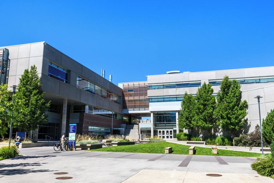 A modern building with a glass facade, a grassy courtyard, and a few trees.