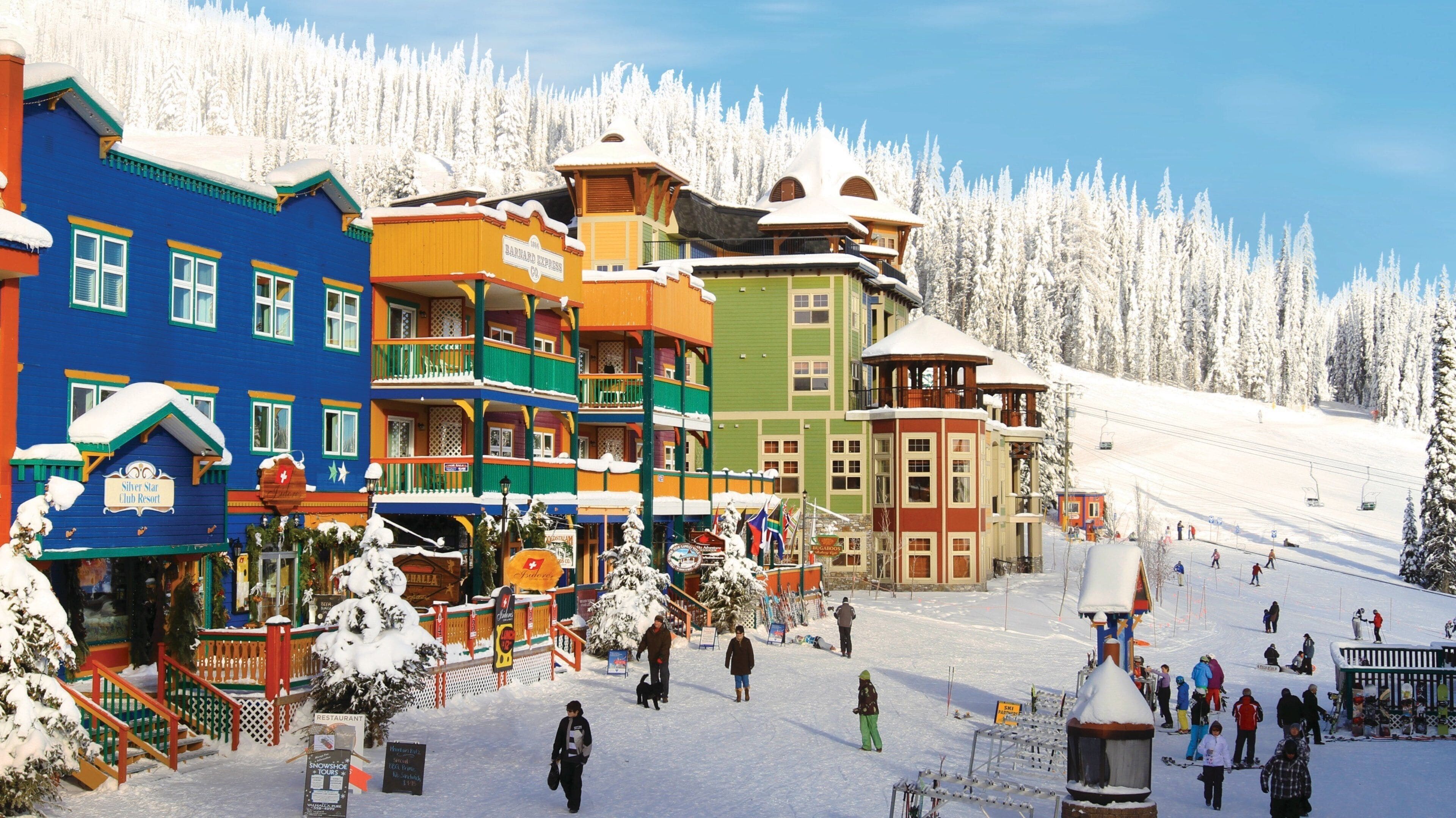 Edifici colorati, una pista da sci e alberi innevati.