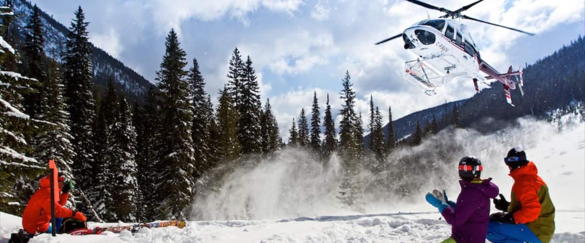 A helicopter flying over a snowy mountain area with skiers on the ground.