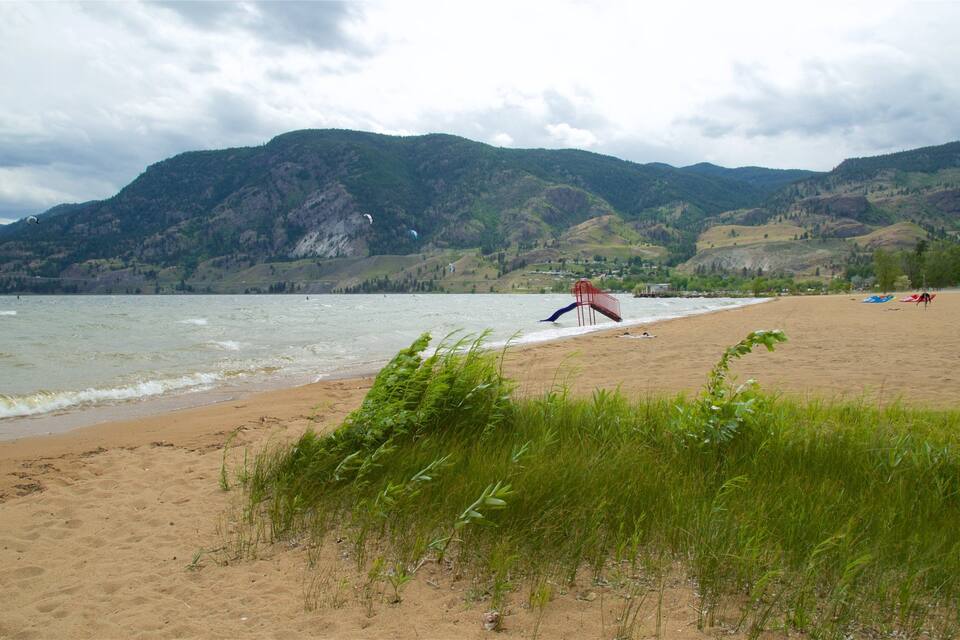 Une plage avec une chaise rouge, un rivage sablonneux et des montagnes en arrière-plan.