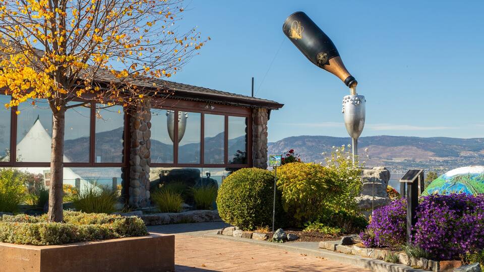 A building with a stone facade, a large sculpture of a bottle, and a view of mountains in the background.