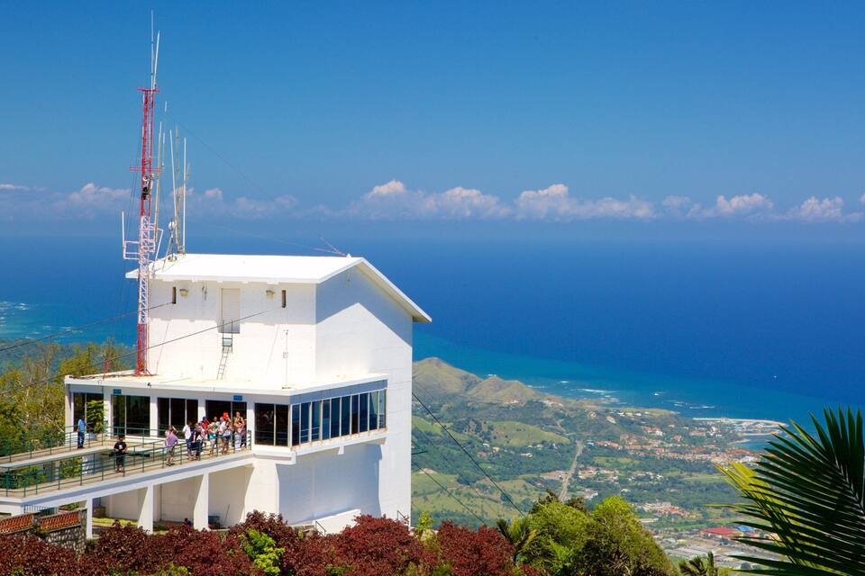 A white observation tower with a red antenna, overlooking a coastal landscape with hills and a clear blue sky.