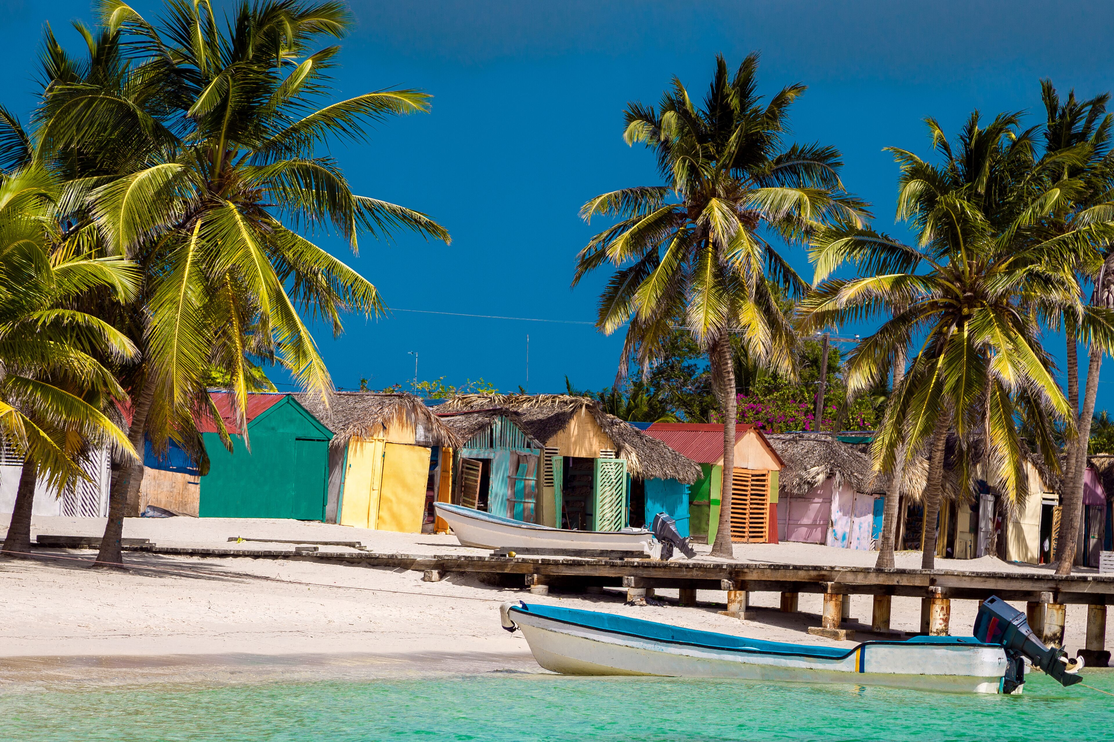 A beach with palm trees, colorful buildings, and boats.