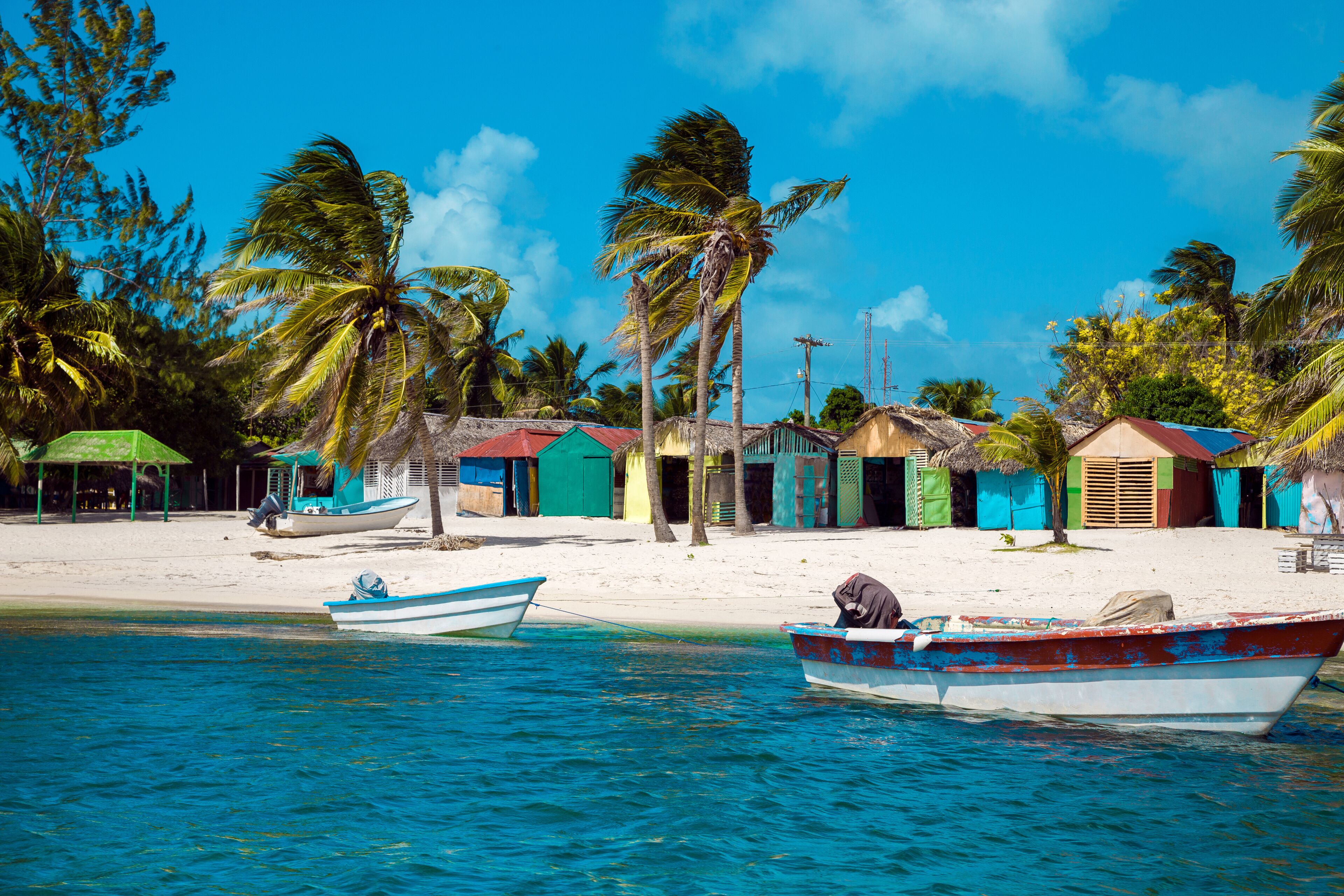 A beach with two boats, palm trees, and colorful buildings.
