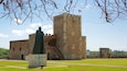 A historic castle with a statue in front, a flag on top, and a clear sky.