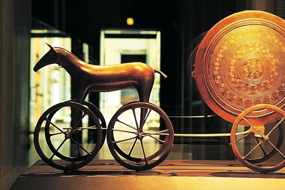 Un carro tirat per cavalls de fusta amb rodes ornamentades i una placa decorativa.