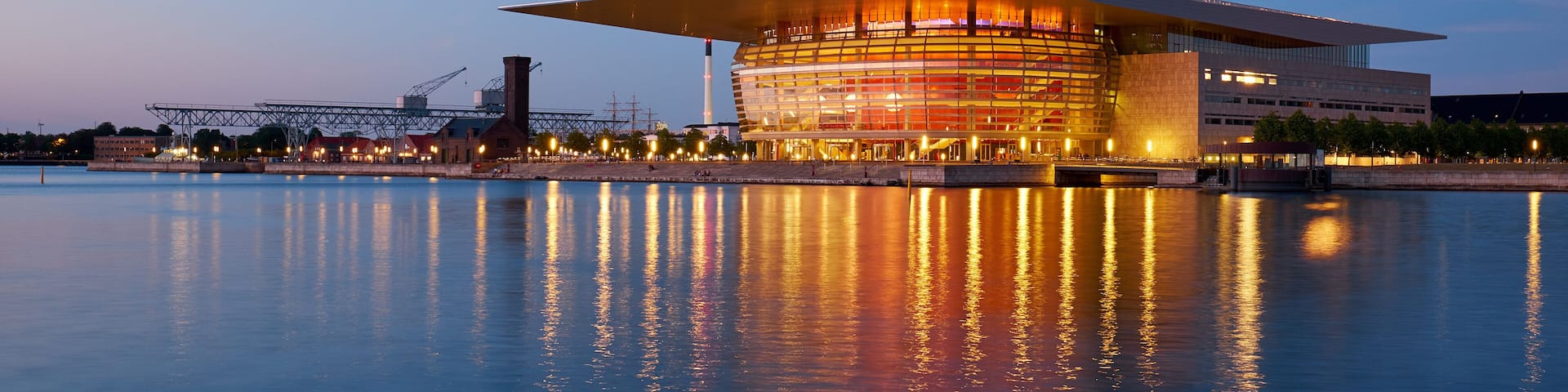A modern building with a unique architectural design, situated by a calm body of water reflecting the structure.