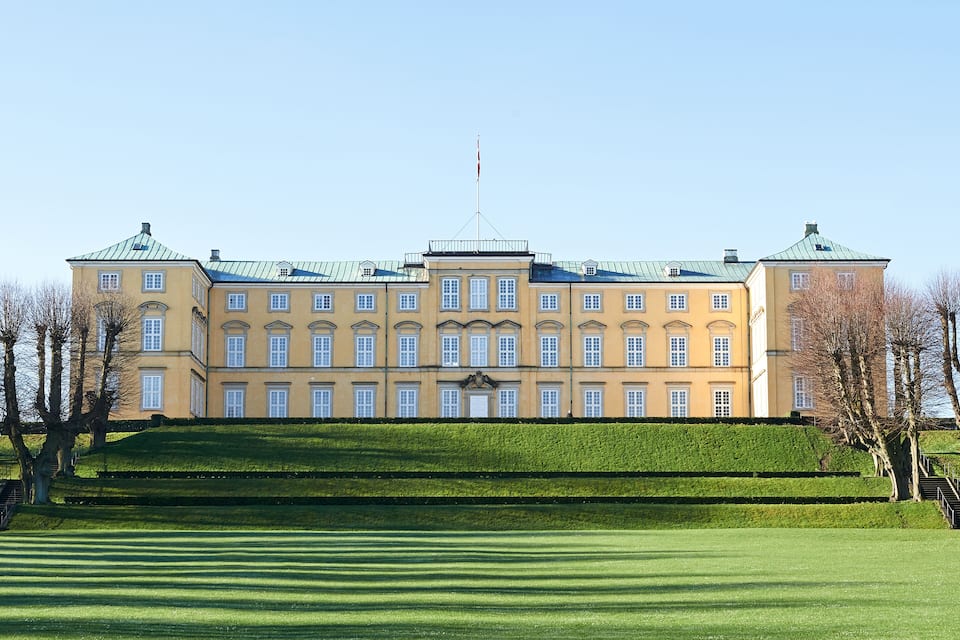 A large, yellow building with a green roof, surrounded by a well-manicured lawn and trees.