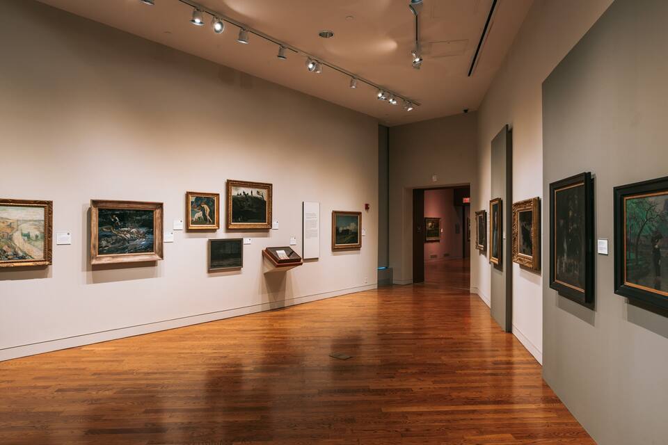Eine Kunstgalerie mit Holzböden und Gemälden an den Wänden.