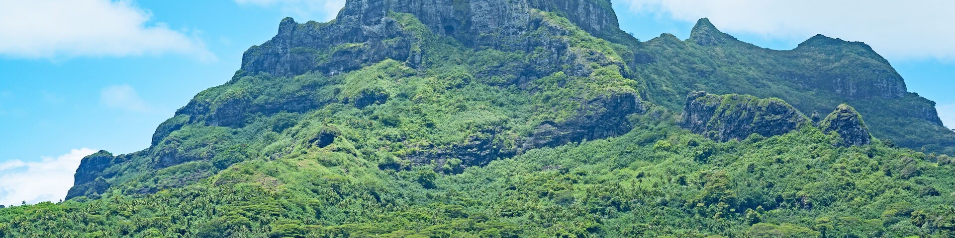 Paisagem montanhosa com um pico imponente, um corpo de água em primeiro plano e edifícios dispersos ao longo da costa.
