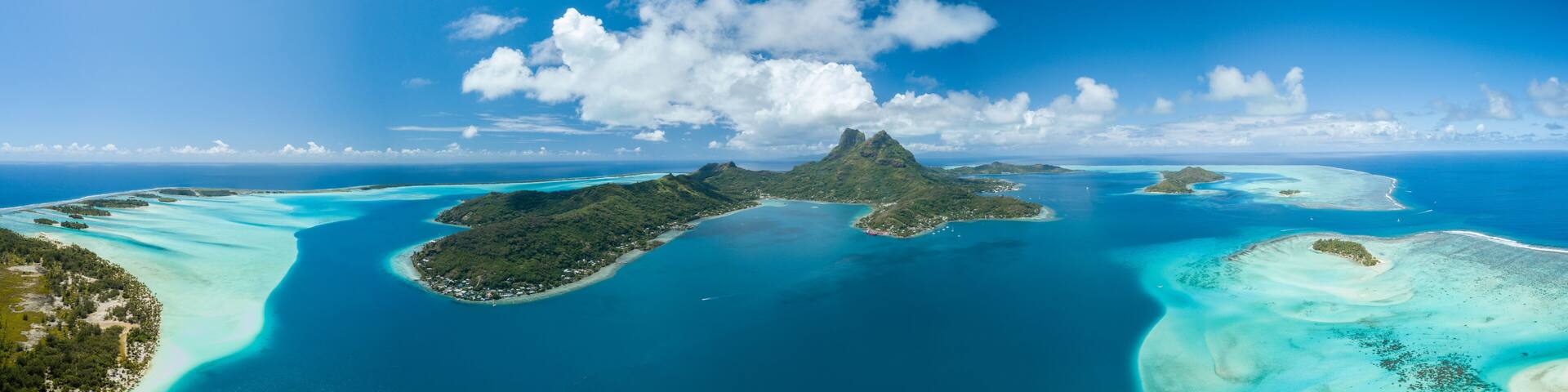 Panoramic aerial view of luxury overwater villas with palm trees, blue lagoon, white sandy beach and Otemanu mountain at Bora Bora island, Tahiti, French Polynesia (Bora Bora Aerial)