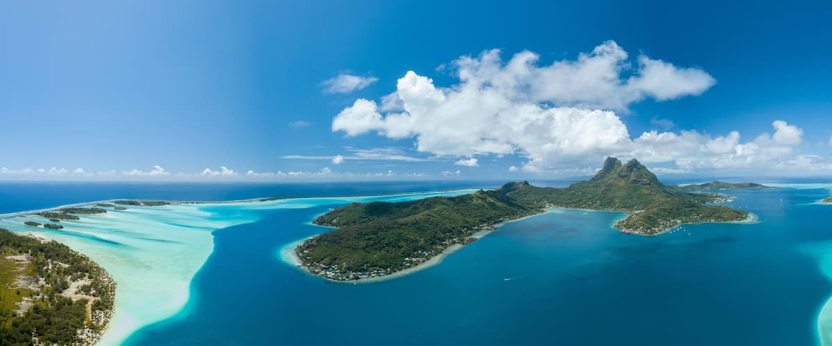 A tropical island landscape with clear turquoise waters, a prominent mountain peak, and lush greenery.