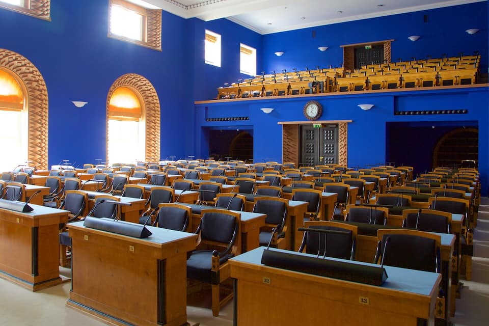 A large hall with blue walls, wooden desks, and chairs arranged in rows.