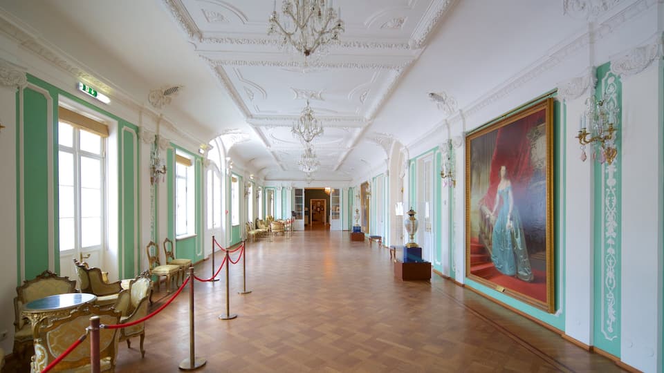 A grand hallway with ornate chandeliers, green and white walls, and classical furniture.