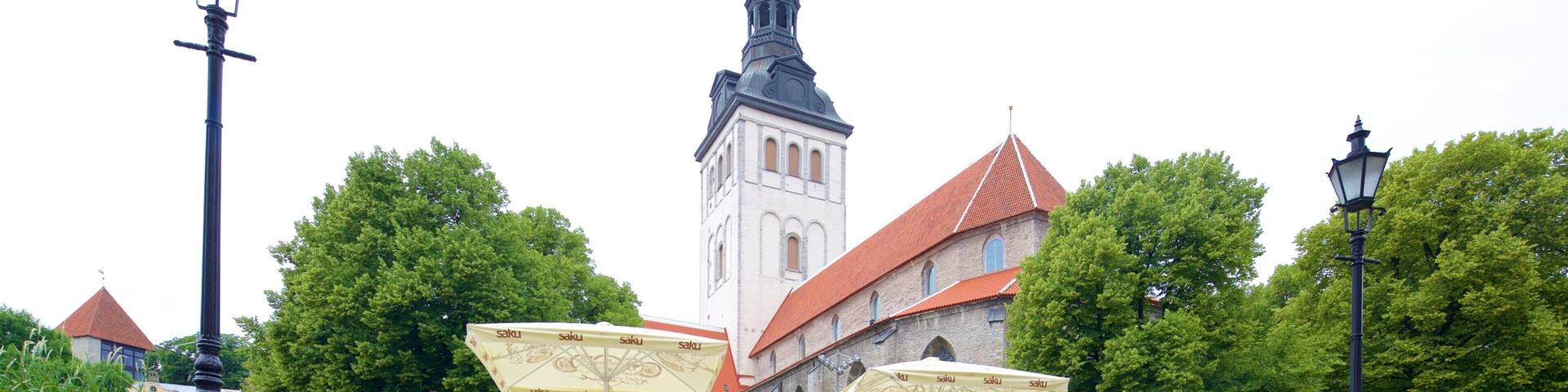 A historic building with a tower, surrounded by lush green trees and outdoor seating areas with umbrellas.