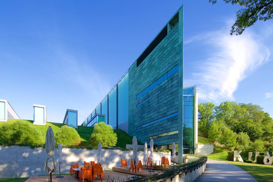 Un edificio moderno con tetto spiovente e ampie finestre, immerso nel verde e con area salotto all'aperto.