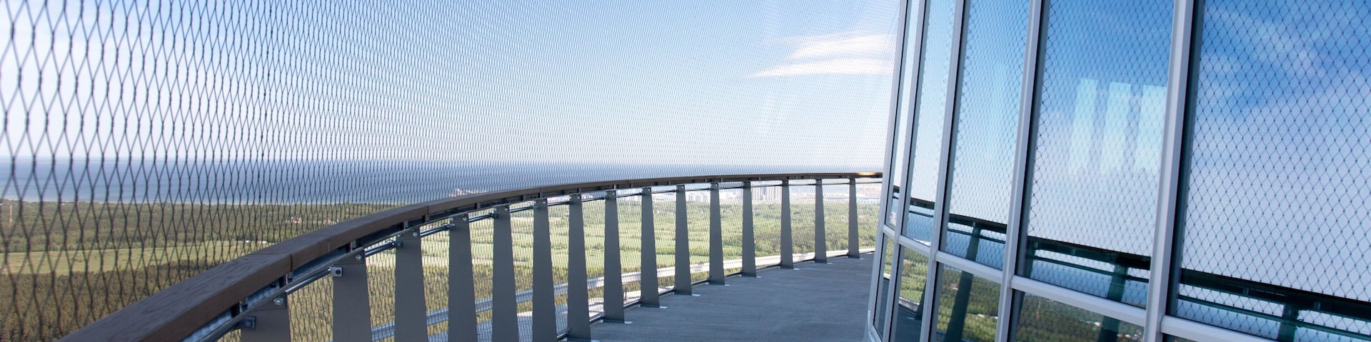 Uma estrutura arquitetônica moderna com fachada de vidro e guarda-corpos de metal, com vista para a paisagem.