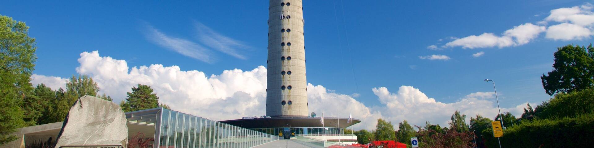 A tall tower with circular windows, a glass bridge, and a stone monument.
