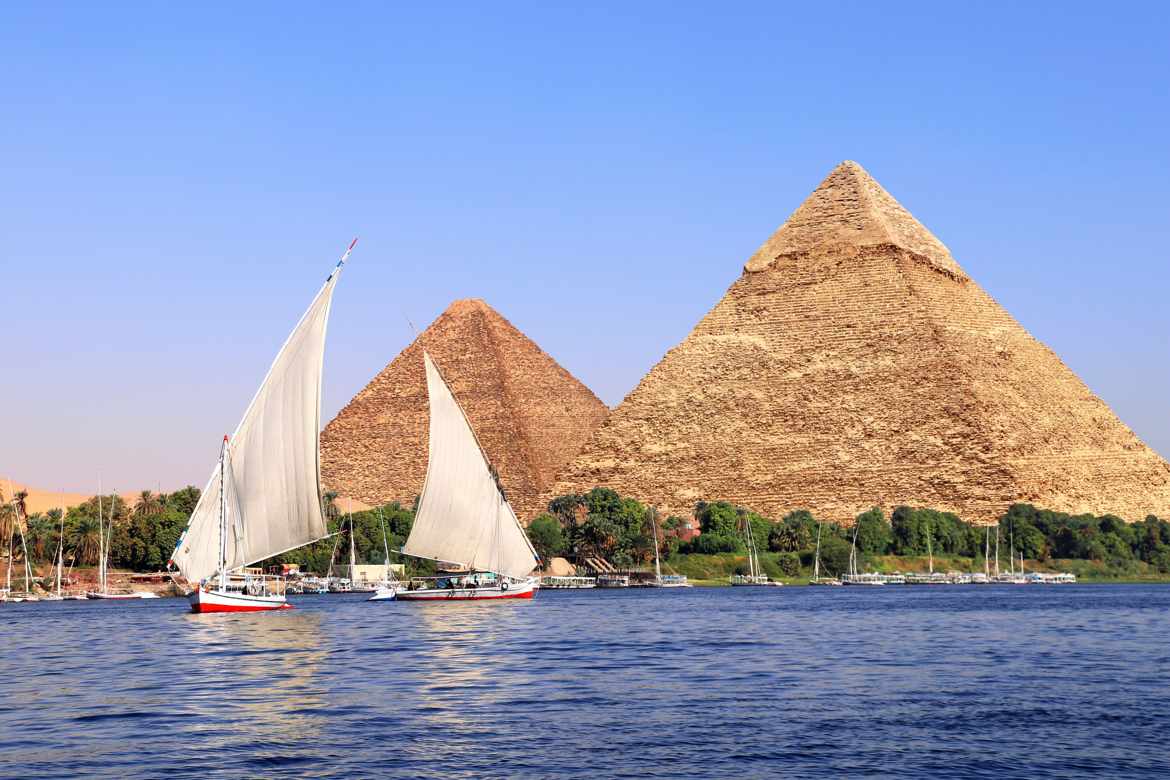 Great Pyramids of Chephren and Cheops and traditional sailing boat felucca, Nile river, Egypt. Famous tourist attraction sailing boat ride. Topic of travel, trip abroad on vacation, cruises and tours