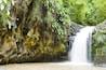 Een waterval die over rotsachtig terrein stroomt, met weelderige begroeiing.