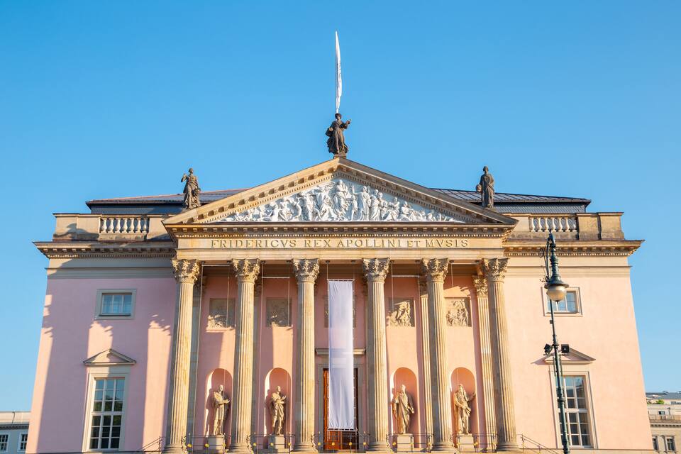 A classical building with columns and statues, including a prominent figure holding a flag.