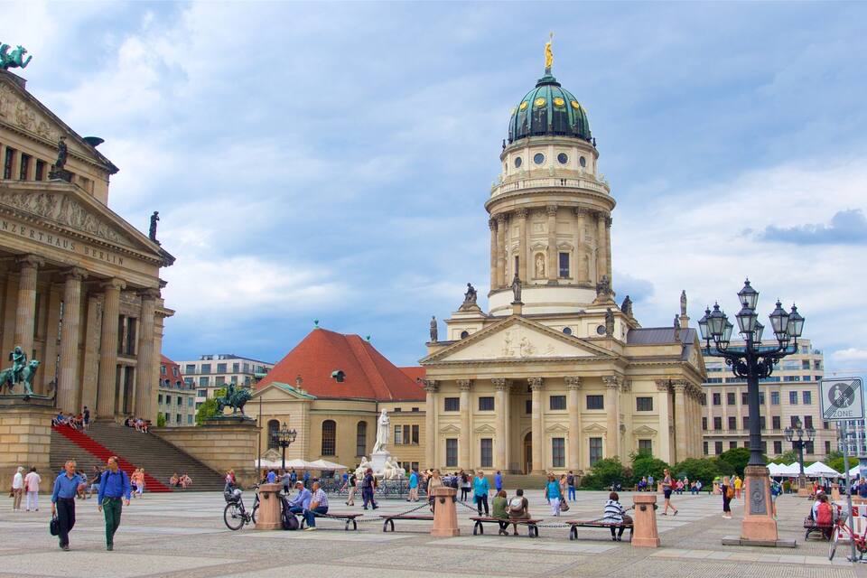 A large open square with a prominent building featuring a green dome and classical architecture.