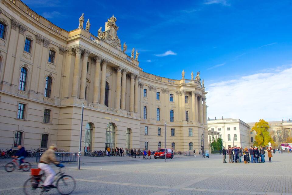 A historic building with classical architecture, a clear blue sky, and people walking in the foreground.