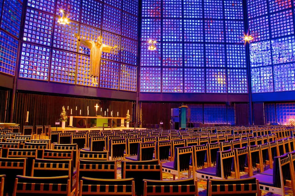 Un amplio salón con hileras de sillas y un escenario con una cruz y velas.