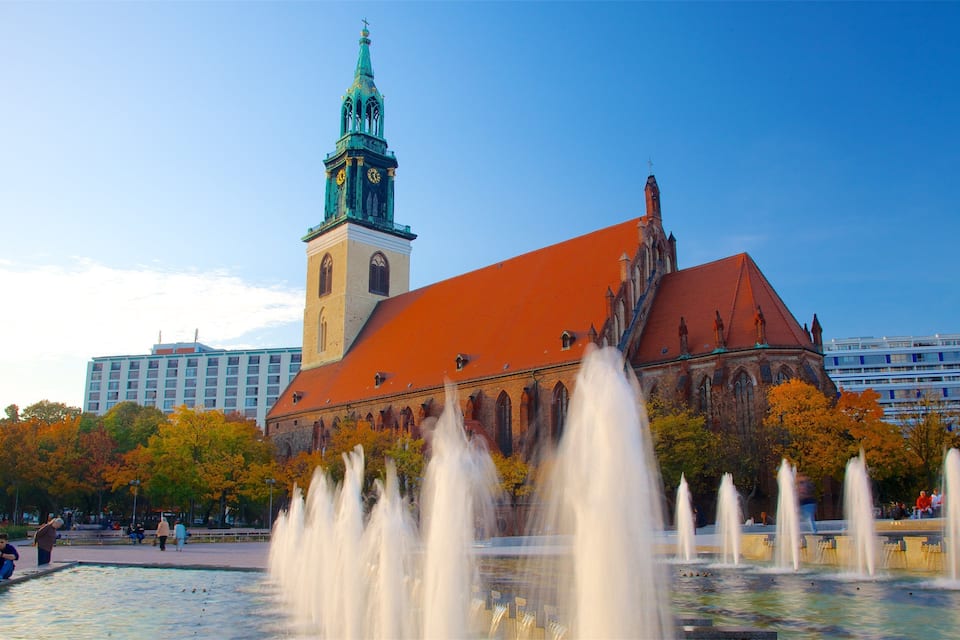 A historic church with a clock tower, surrounded by autumn trees and a fountain.