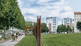 Een park met een moderne sculptuur, een pad en stadsgebouwen op de achtergrond.