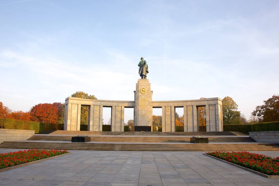 A large monument with a statue in the center, surrounded by steps and red flowers.