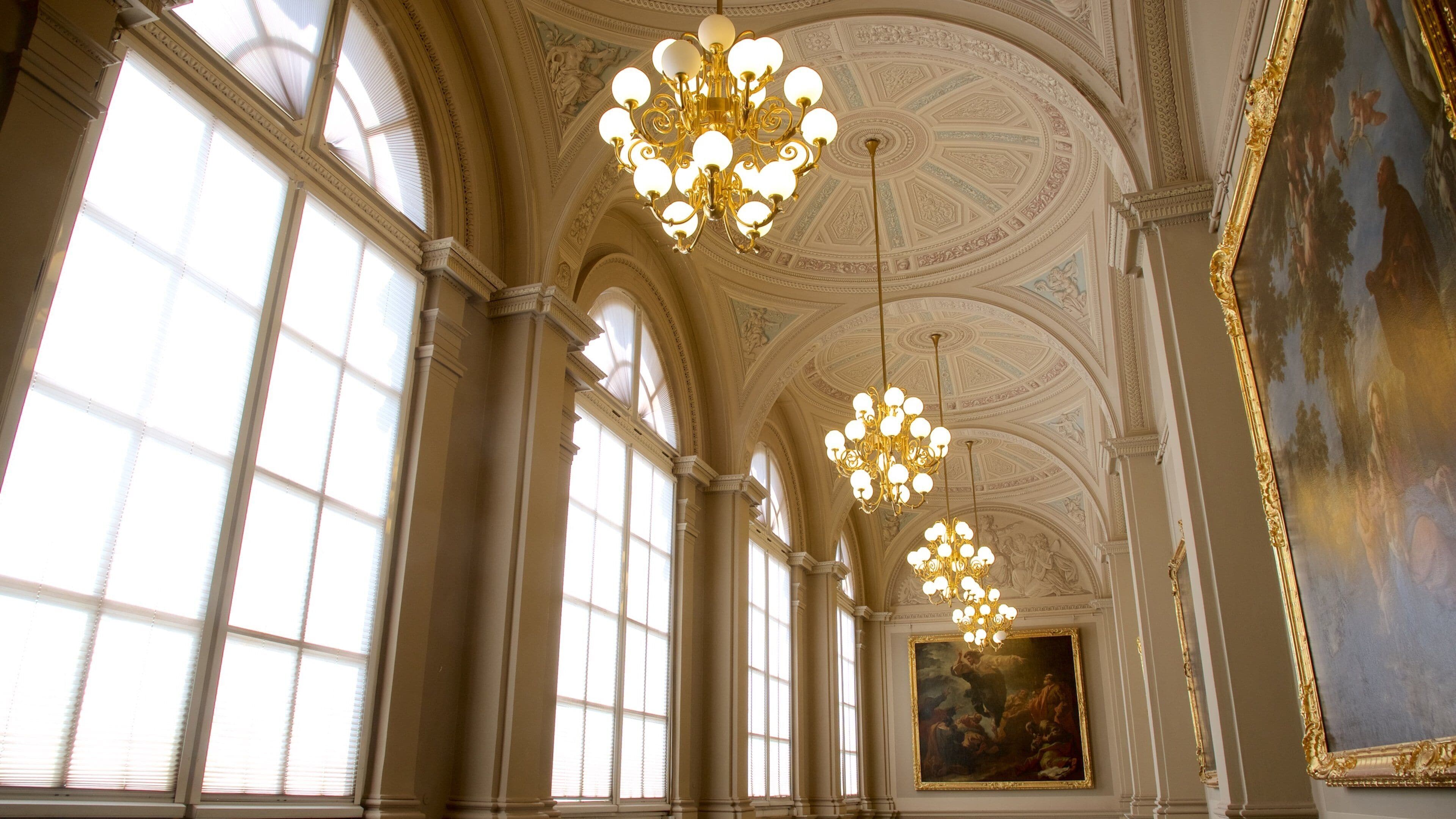 Un salón imponente con amplias ventanas de arco, candelabros ornamentados y un techo de estilo clásico.