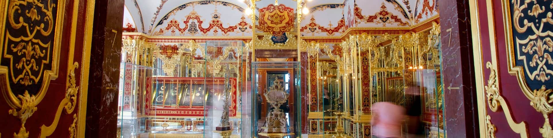 An ornate room with gold and red decorations, a checkered floor, and a glass display case.