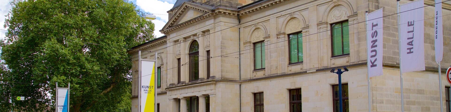 Un edificio clásico con contraventanas verdes, una escultura y banderines.