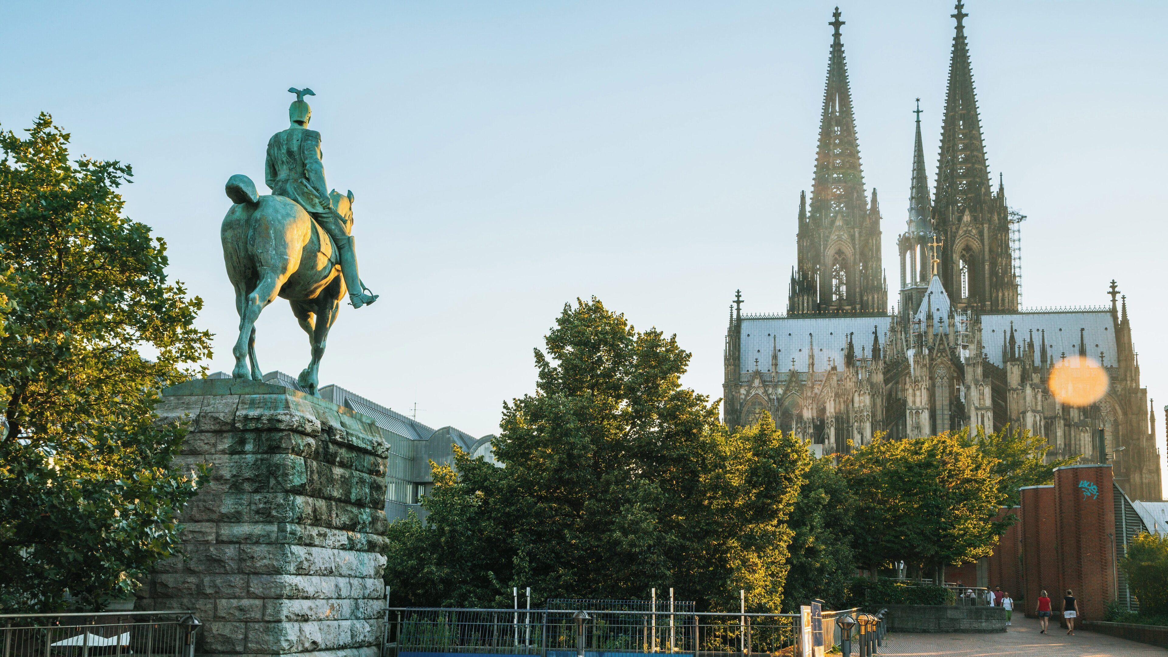Cologne Cathedral stands majestically in Altstadt-Nord while a bronze statue of a knight overlooks the vibrant city in North Rhine-Westphalia, Germany at sunset