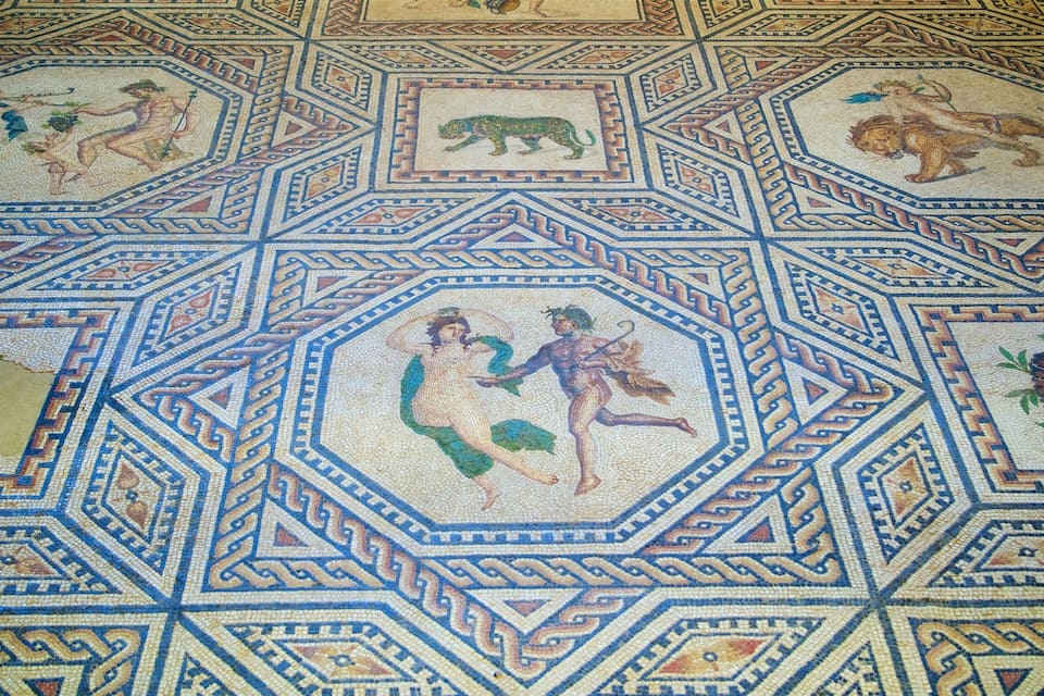 Un detallado suelo de mosaico con patrones geométricos y figuras mitológicas.
