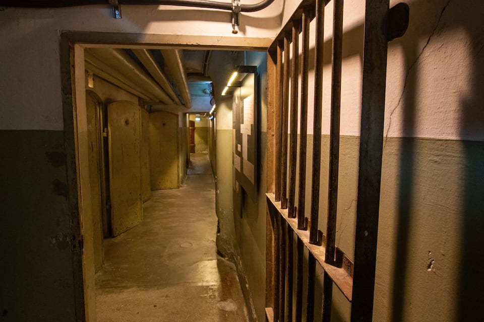 Un passadís poc il·luminat amb portes reixades i un sòl de formigó.