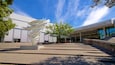 A modern building with a spiral sculpture in front, a tree, and a clear blue sky.