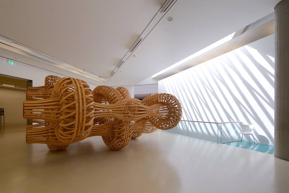 Eine große Holzskulptur in einer modernen Galerie mit minimalistischer Gestaltung.
