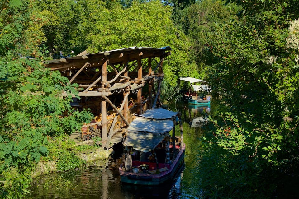 Een traditionele houten boot met rieten dak vaart over een smalle rivier omringd door weelderige begroeiing.