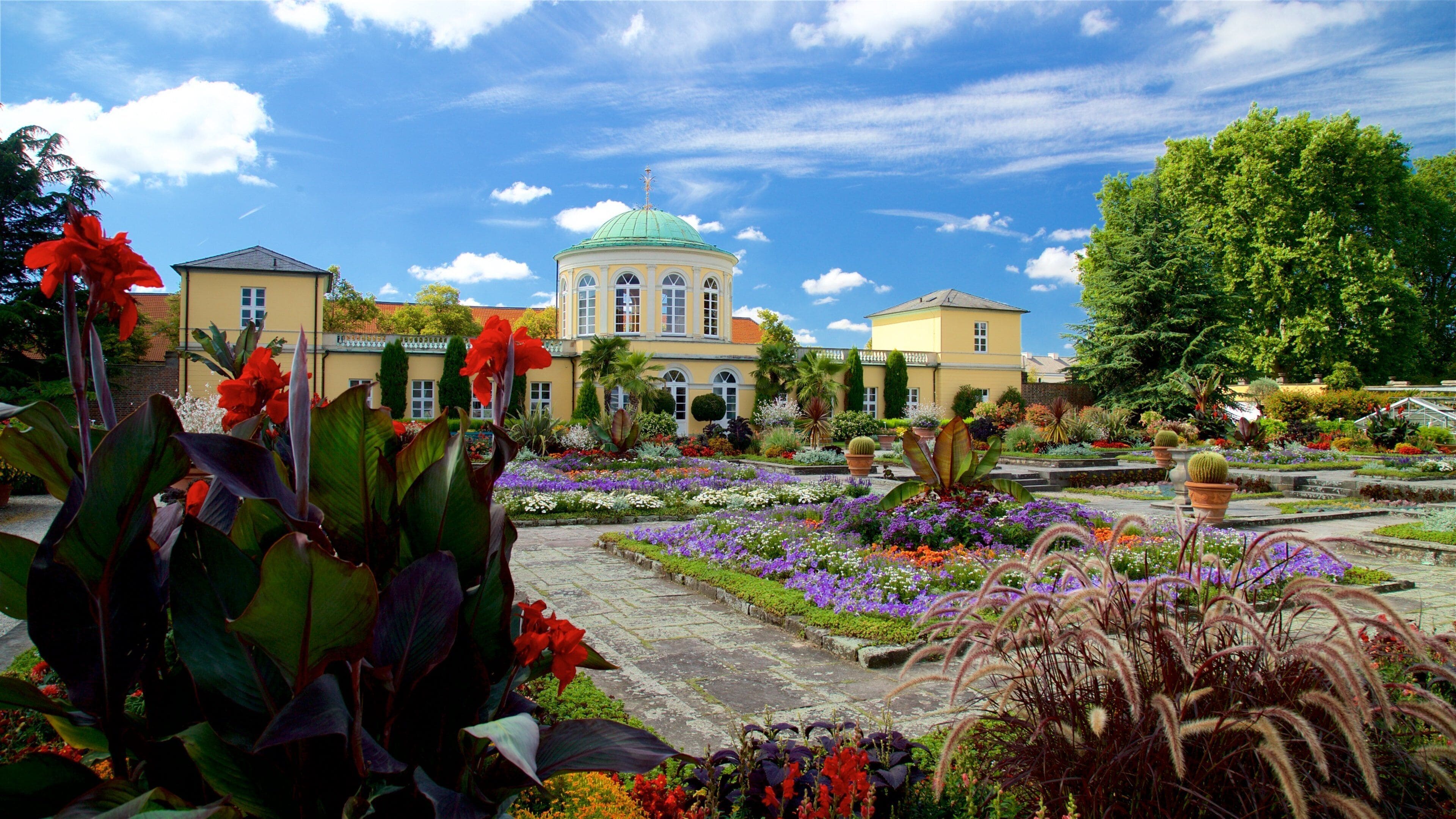 Um jardim com um edifício amarelo, uma cúpula verde e diversas plantas.