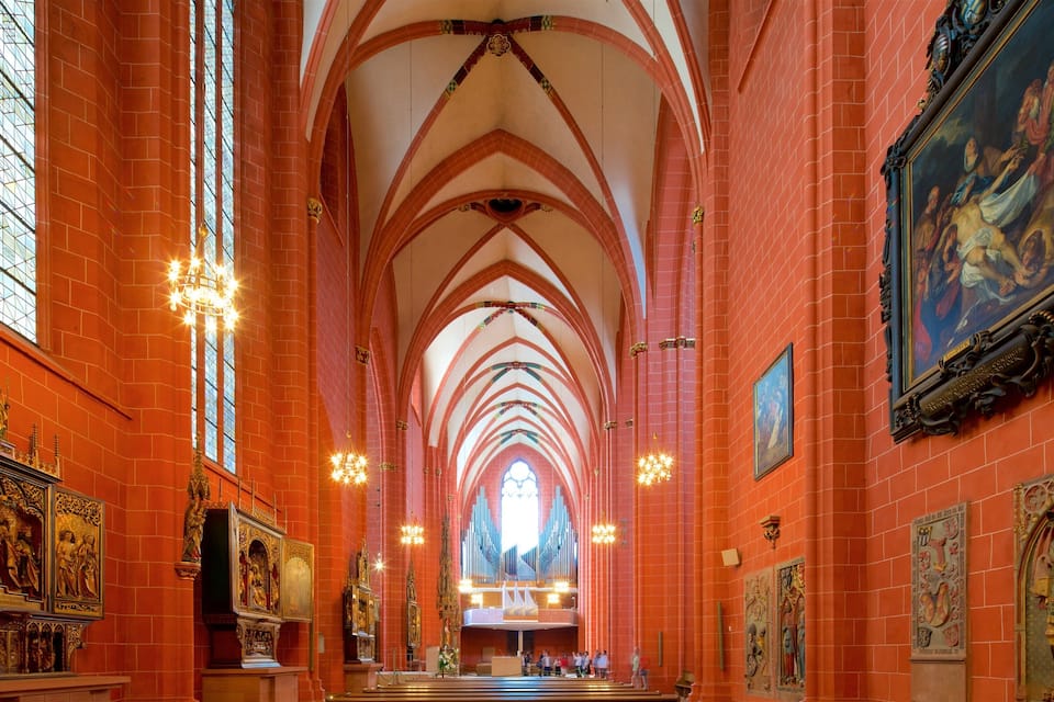 A cathedral interior with red brick walls, arched ceilings, and ornate religious paintings.
