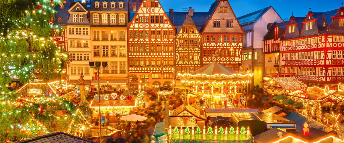 Un marché de Noël avec des bâtiments traditionnels à colombages et un clocher d’église imposant.