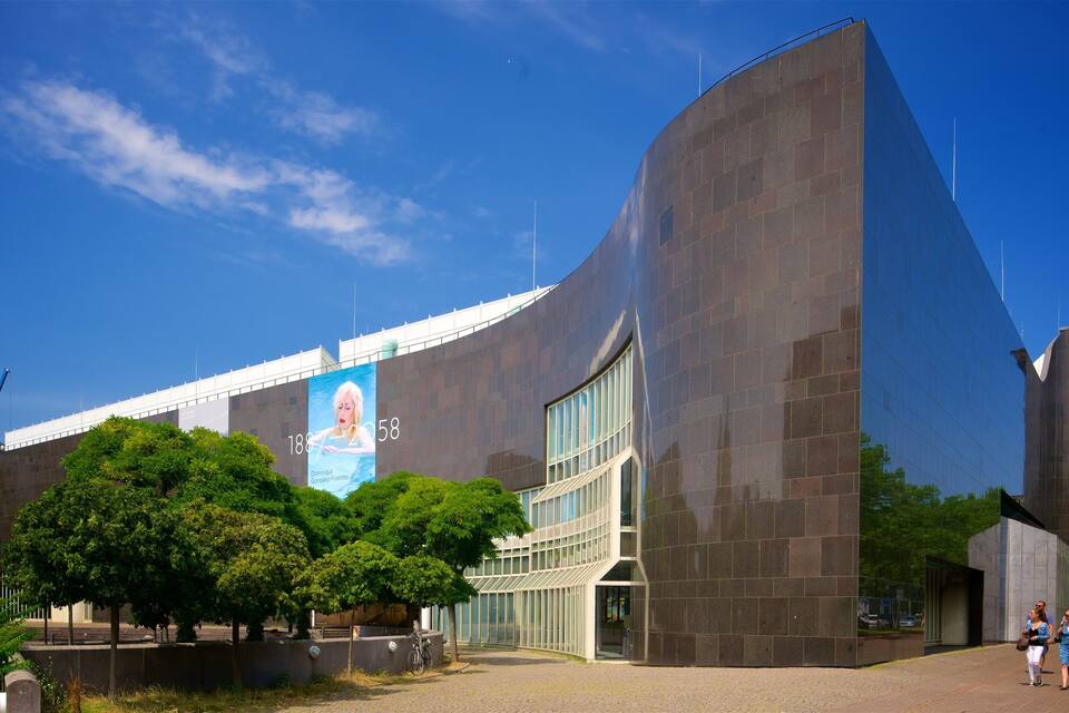A modern building with a large billboard, trees, and a clear blue sky.