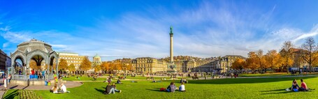 Ein Park mit einer weitläufigen Wiese, einem markanten Denkmal und historischen Gebäuden im Hintergrund.
