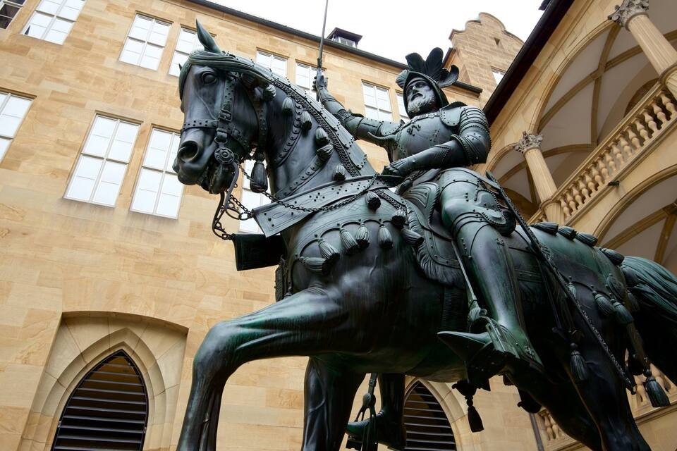 Una estàtua d'un cavaller a cavall davant d'un edifici amb finestres allargassades i un balcó.