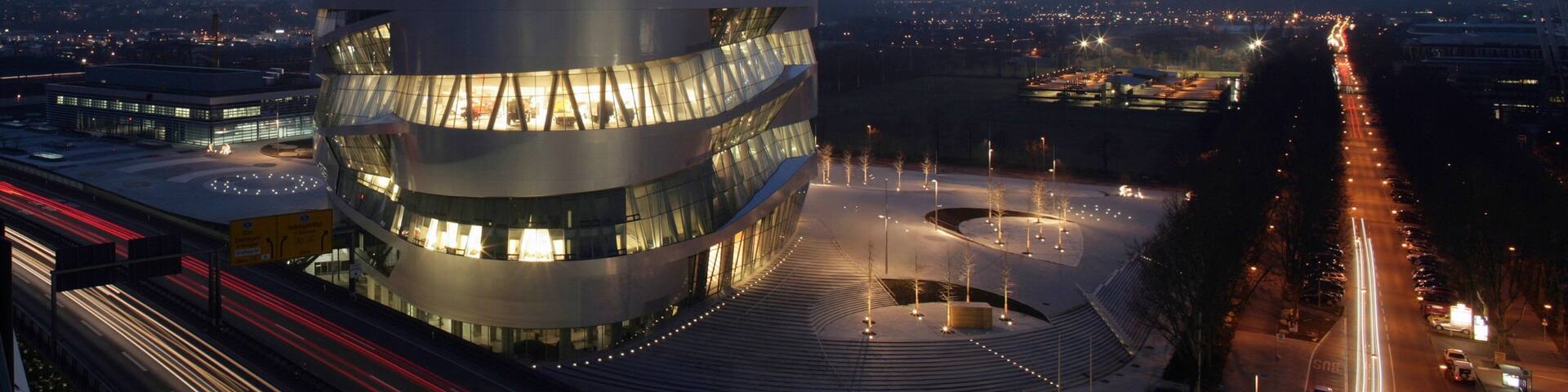 A modern building with a curved facade, surrounded by a parking area and a road with light trails.