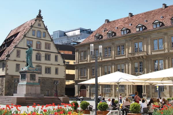 A historic square with a statue, flower beds, and outdoor seating areas.