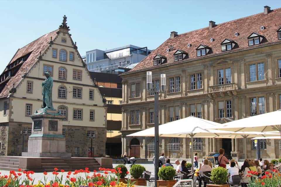 Une place historique agrémentée d’une statue, de parterres de fleurs et d’espaces aménagés pour s’asseoir en plein air.