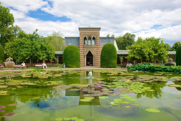 Ein historisches Gebäude mit einem Turm, umgeben von einem Teich mit Seerosen und einem gepflegten Garten.